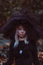 A woman in an oversized hat amidst autumn leaves evokes a moody mystery