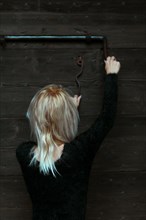 Back view of a blonde thin woman dressed in black reaching up to a rusty antique metal lock on a