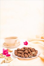 Almond in chocolate dragees on ceramic plate and a cup of coffee on white concrete background and