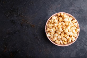 Popcorn with caramel in ceramic bowl on a black concrete background. Top view, flat lay, copy space