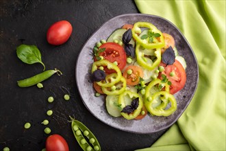 Vegetarian salad from green pea, tomatoes, pepper and basil on a black concrete background and