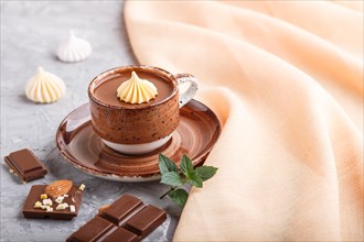 Cup of hot chocolate and pieces of milk chocolate with almonds on a gray concrete background with