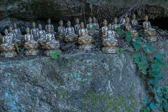 Miniature sitting Buddhas on ledge of boulder in mountainous public park in South Korea