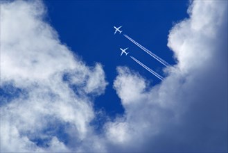 Two white passenger airplanes with vapor trails in blue sky