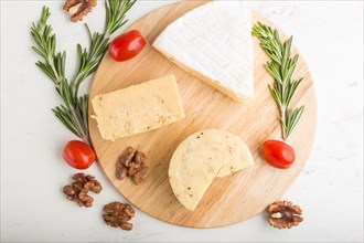 Cheddar and various types of cheese with rosemary and tomatoes on wooden board on a white wooden