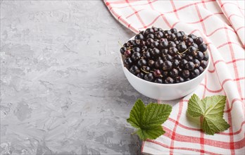 Fresh black currant in white bowl and linen textile on gray concrete background. side view, close
