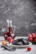 Black potato chips with charcoal, balsamic vinegar in glass, red grapes on a blue ceramic plate on