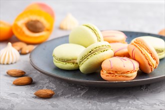 Orange and green macarons or macaroons cakes on blue ceramic plate on a gray concrete background.