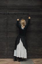 Full body shot of a young blonde caucasian woman reaching an antique lock of a wooden door above