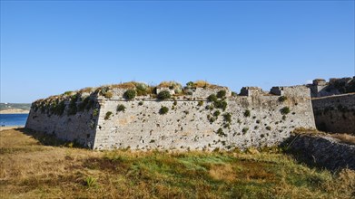 Part of the ruins of a stone fortress with grassy areas in front, sea fortress Methoni,