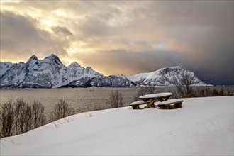 Eine verschneite Bank vor dem Sonnenuntergang mit Bergen auf den Vesteralen