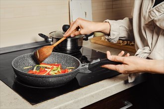 Unrecognizable woman stirring vegetable dressing with wooden spatula in frying pan