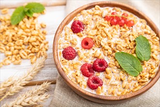 Wheat flakes porridge with milk, raspberry and currant in wooden bowl on white wooden background