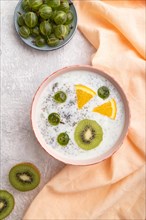 Yogurt with kiwi, gooseberry, chia in ceramic bowl on gray concrete background and orange linen