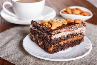 Chocolate cake with caramel, peanuts and almonds on a brown wooden background. cup of coffee, close