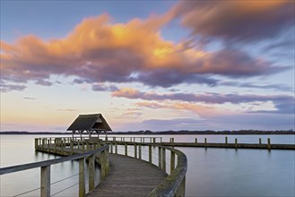 The well-known curved wooden footbridge in the evening light with pink clouds on Lake Hellendorf as