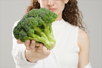 Unrecognizable woman holding broccoli in her outstretched hand, focus on foreground