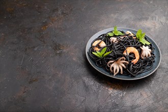 Black cuttlefish ink pasta with shrimps or prawns and small octopuses on black concrete background.