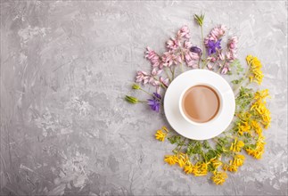 Yellow, pink and blue flowers in a spiral and a cup of coffee on a gray concrete background.