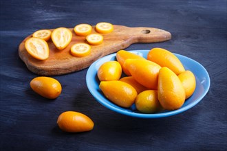Kumquats in a blue plate on a black wooden background, close up