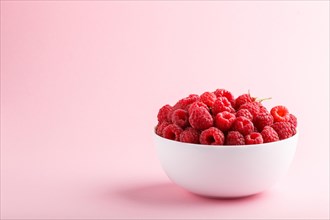 Fresh raspberry in white bowl on pink pastel background. side view, copy space