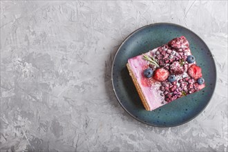 Berry cake with milk cream and blueberry jam on blue ceramic plate on a gray concrete background.