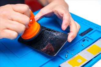 Close-up of the hands of a repairman using a suction cup to lift a broken screen of a mobile phone