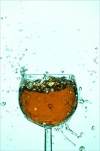 Splashing liquid in orange and turquoise in a wine glass, blue background