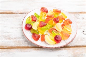 Various fruit jelly candies on plate on white wooden background. side view, close up