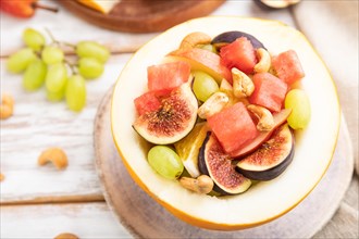 Vegetarian fruit salad of watermelon, grapes, figs, pear, orange, cashew on white wooden background