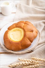 Sour cream bun with cup of coffee on a white wooden background and linen textile. Side view, close