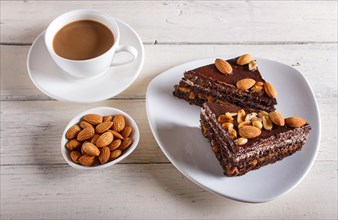 Chocolate cake with caramel, peanuts and almonds on a white wooden background. cup of coffee, top