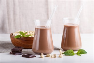 Organic non dairy cashew chocolate milk in glass and wooden plate with cashew nuts on a gray