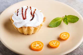Cake with whipped egg cream on a light brown plate with kumquat slices and mint leaves on a gray