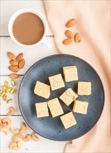Traditional indian candy soan papdi in a blue ceramic plate with almond, pistache, cashew and a cup