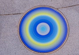 Closeup round glass of blue, yellow and white inlaid in concrete sidewalk in public park in South