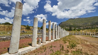 Row of ancient columns in front of mountains and blue sky with fluffy clouds, stadium,