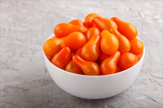 Fresh orange grape tomatoes in white ceramic bowl on gray concrete background. side view, close up