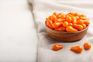 Fresh orange grape tomatoes in wooden bowl on white wooden background with linen napkin. side view,