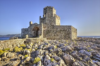 Sunlit castle ruins on a rocky cliff above the sea, octagonal medieval tower. Islet of Bourtzi, sea