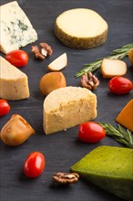 Set of different types of cheese with rosemary and tomatoes on a black wooden background. Side