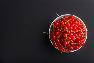 Fresh red currant in white bowl on black background. top view, flat lay, copy space
