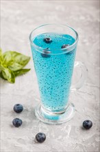 Glass of blueberry blue colored drink with basil seeds on a gray concrete background. Morninig,