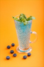 Glass of blueberry blue colored drink with basil seeds on orange background. Morninig, spring,
