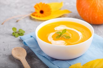 Traditional pumpkin cream soup with in white bowl on a gray concrete background with blue napkin.