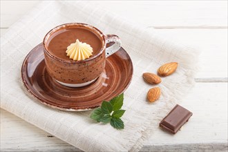 Cup of hot chocolate and pieces of milk chocolate with almonds on a white wooden background with