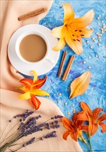Orange day-lily and lavender flowers and a cup of coffee on a blue concrete background, with orange