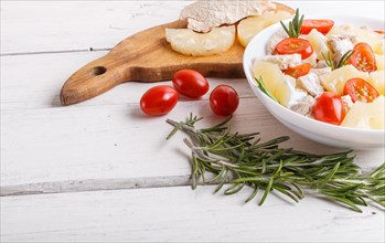 Chicken fillet salad with rosemary, pineapple and cherry tomatoes on white wooden background. close