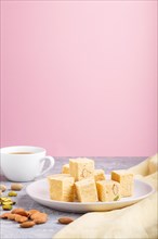 Traditional indian candy soan papdi in white plate with almond, pistache and a cup of coffee on a