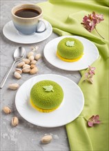 Green mousse cake with pistachio cream and a cup of coffee on a gray concrete background and green